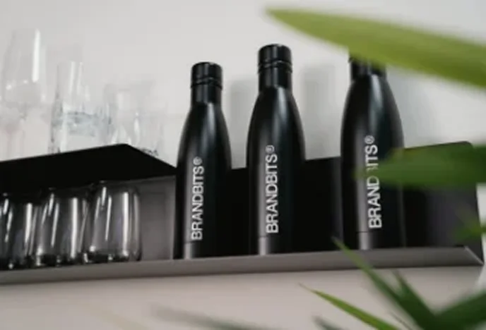 Black Witt's Water bottles are on a shelf next to glasses in the office space.