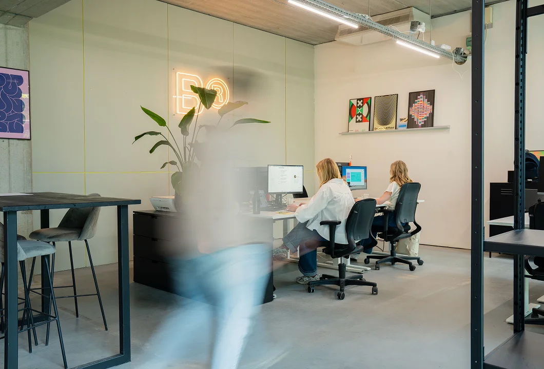 Fieve and Nelle from Brandbits are working behind their computers in the studio, with the illuminated Brandbits logo in the background.