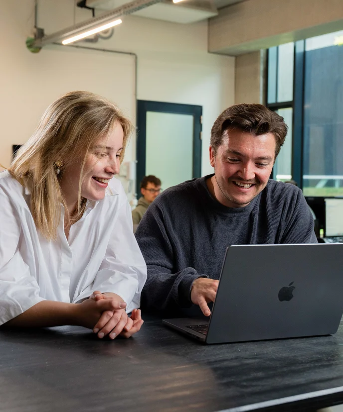 Nelle and Vincent from Brandbits laugh as they work together on a digital project behind a laptop.