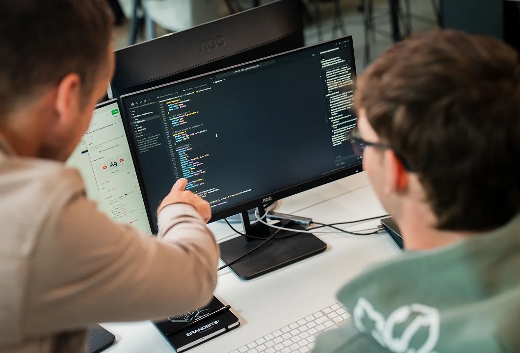 Rik and Toon from Brandbits are looking at code on a computer monitor together as they develop a digital solution.